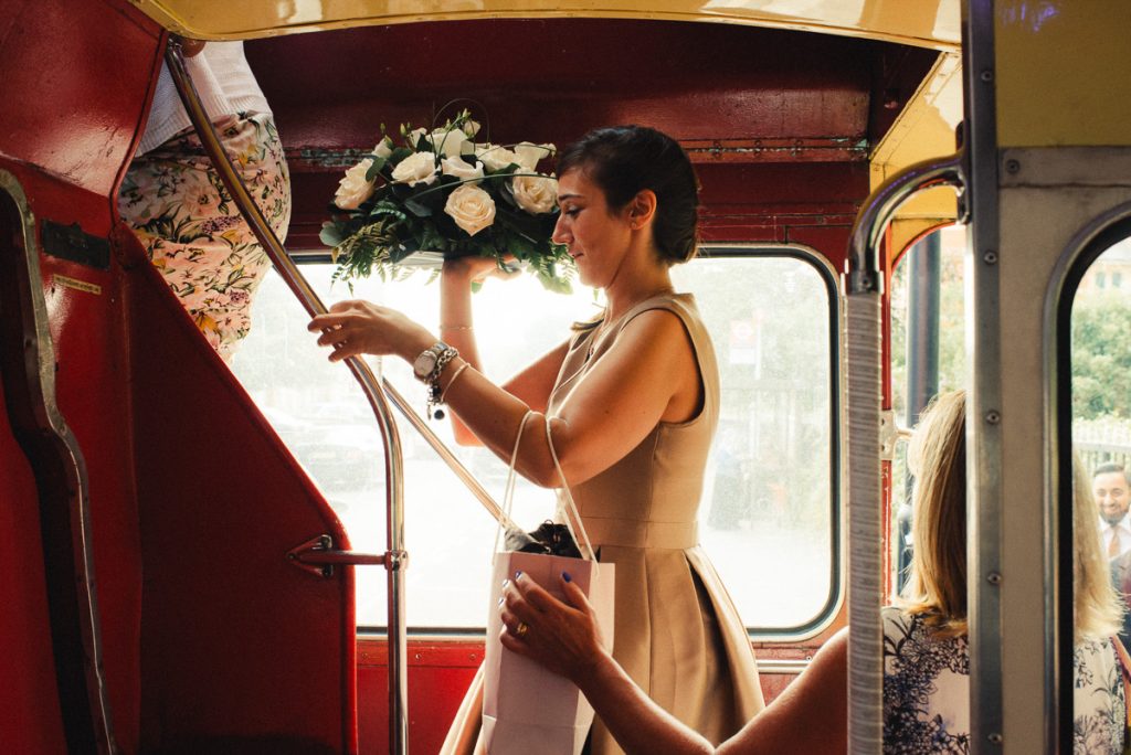 Lady climbing london deck bus with flowers London Wedding